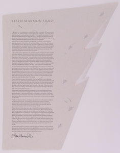 Broadside by Leslie Marmon Silko. Black text on grey handmade paper. The paper is extended out from the top right corner and mimics the shape of a mountain range. On the paper are small tree like shapes scattered around the right side of the paper.